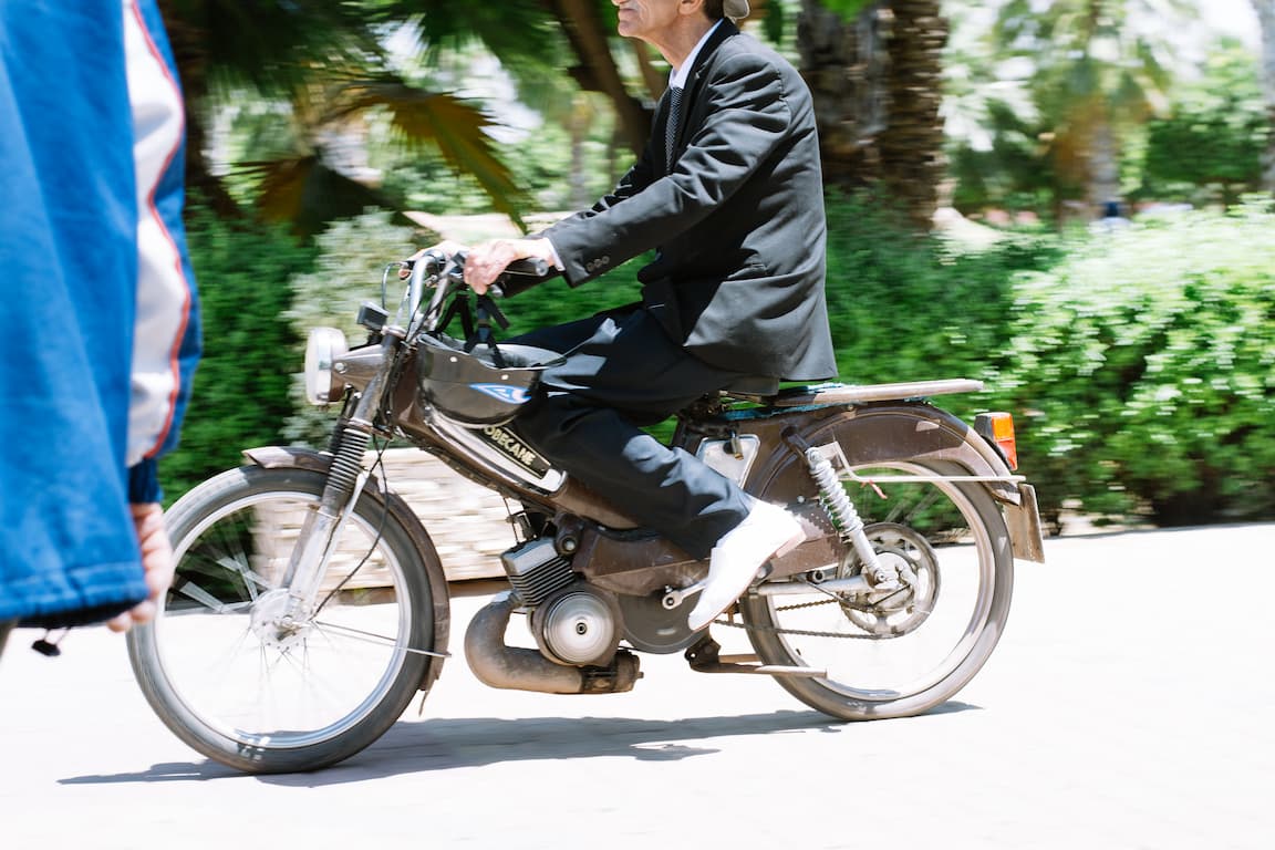 A man in a suit rides by on a motorbike. The background is blurred