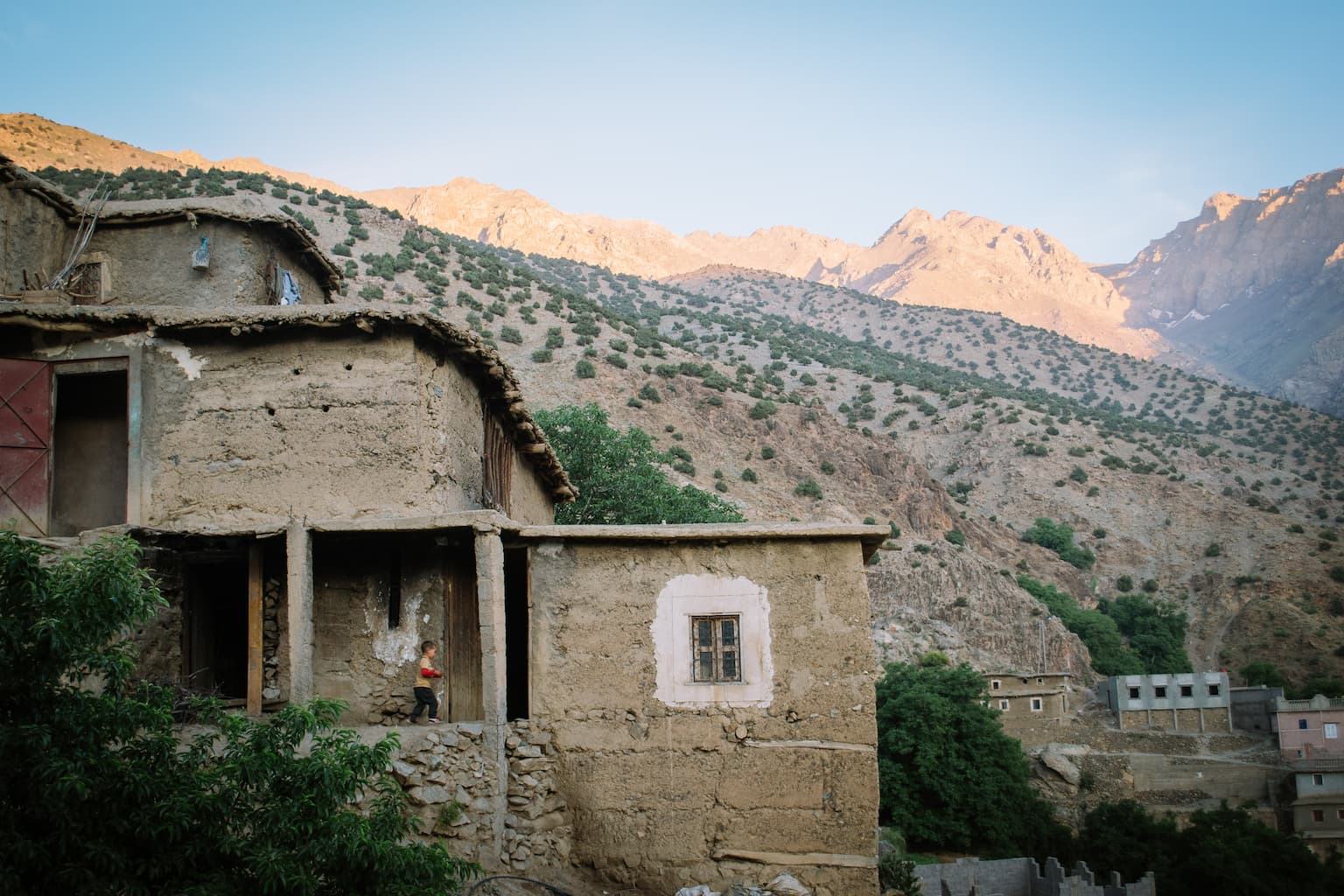 A young boy running past a house with mountains in the background