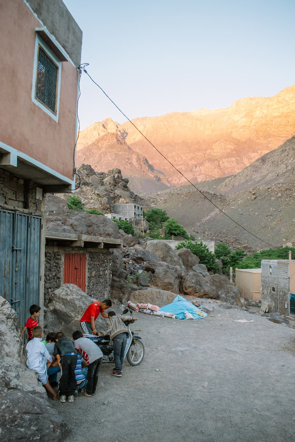 A group of children crowd round a motorbike with mountains in the background