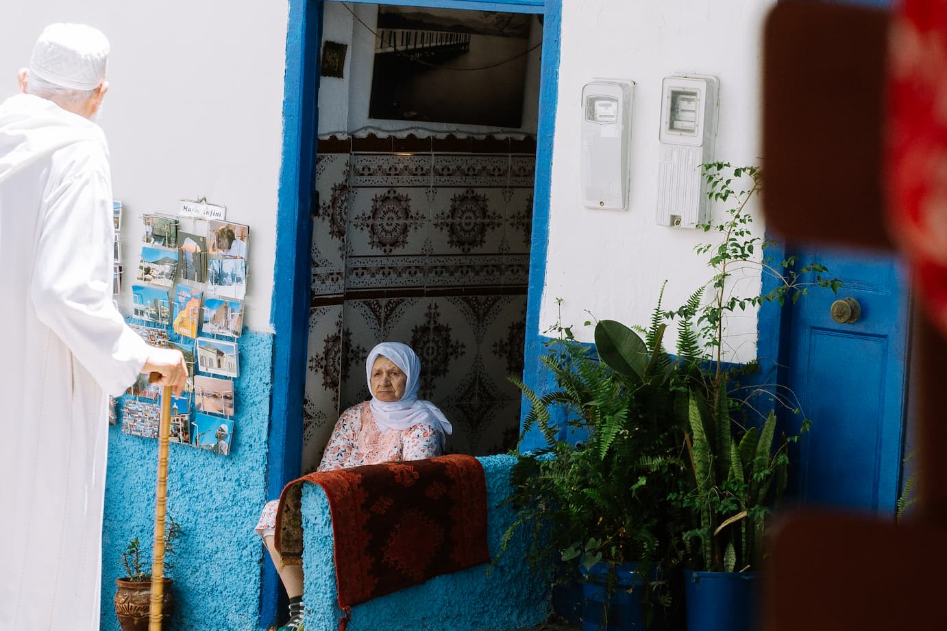 An older woman sits on the front step of a blue house