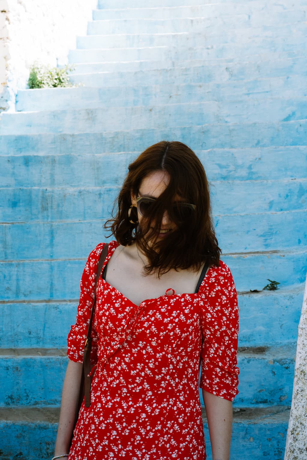 Sarah wearing a red dress, walking down some blue steps, while the wind blows her hair across her face