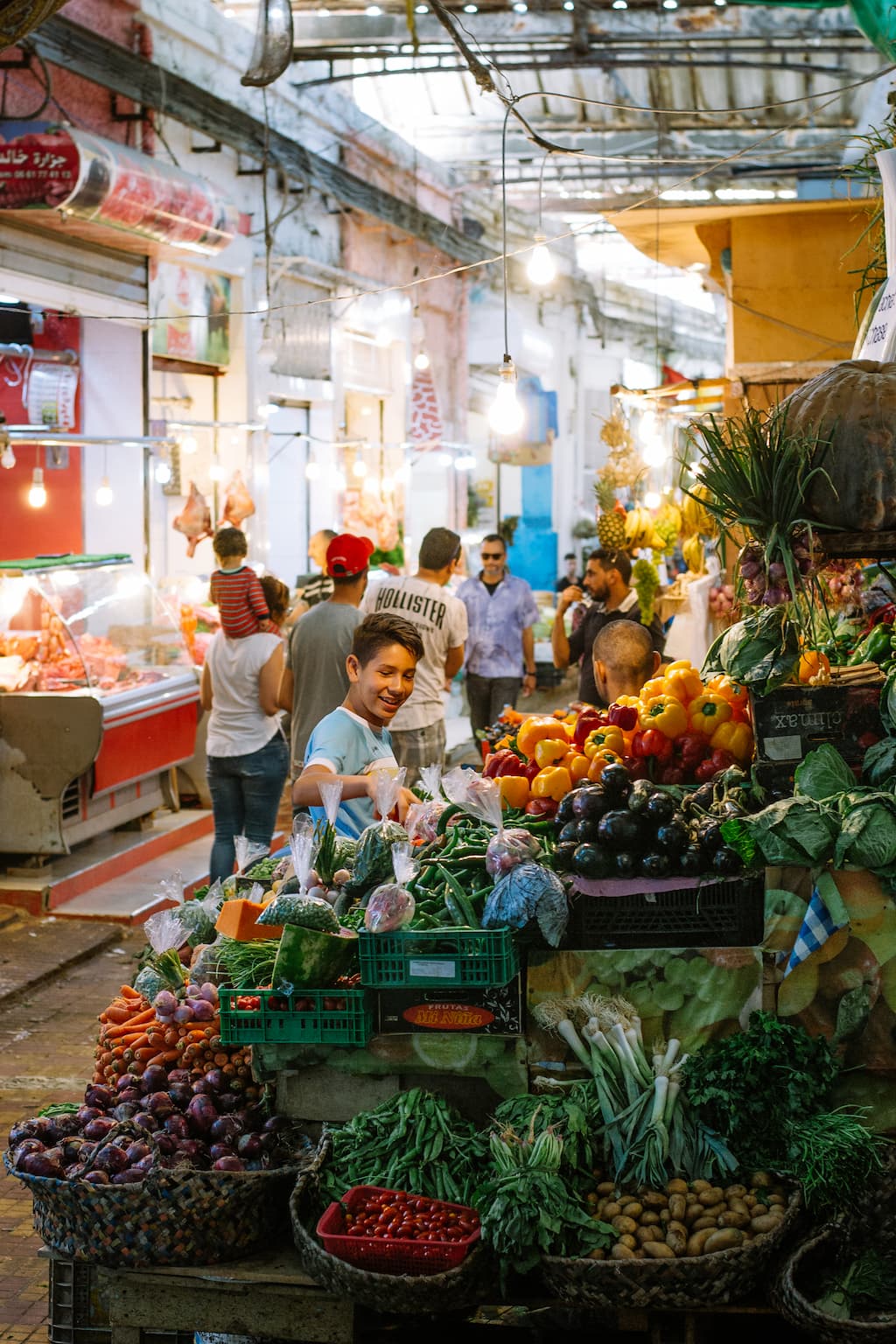 A boy smiles standing at a colourful fruit stall in a market