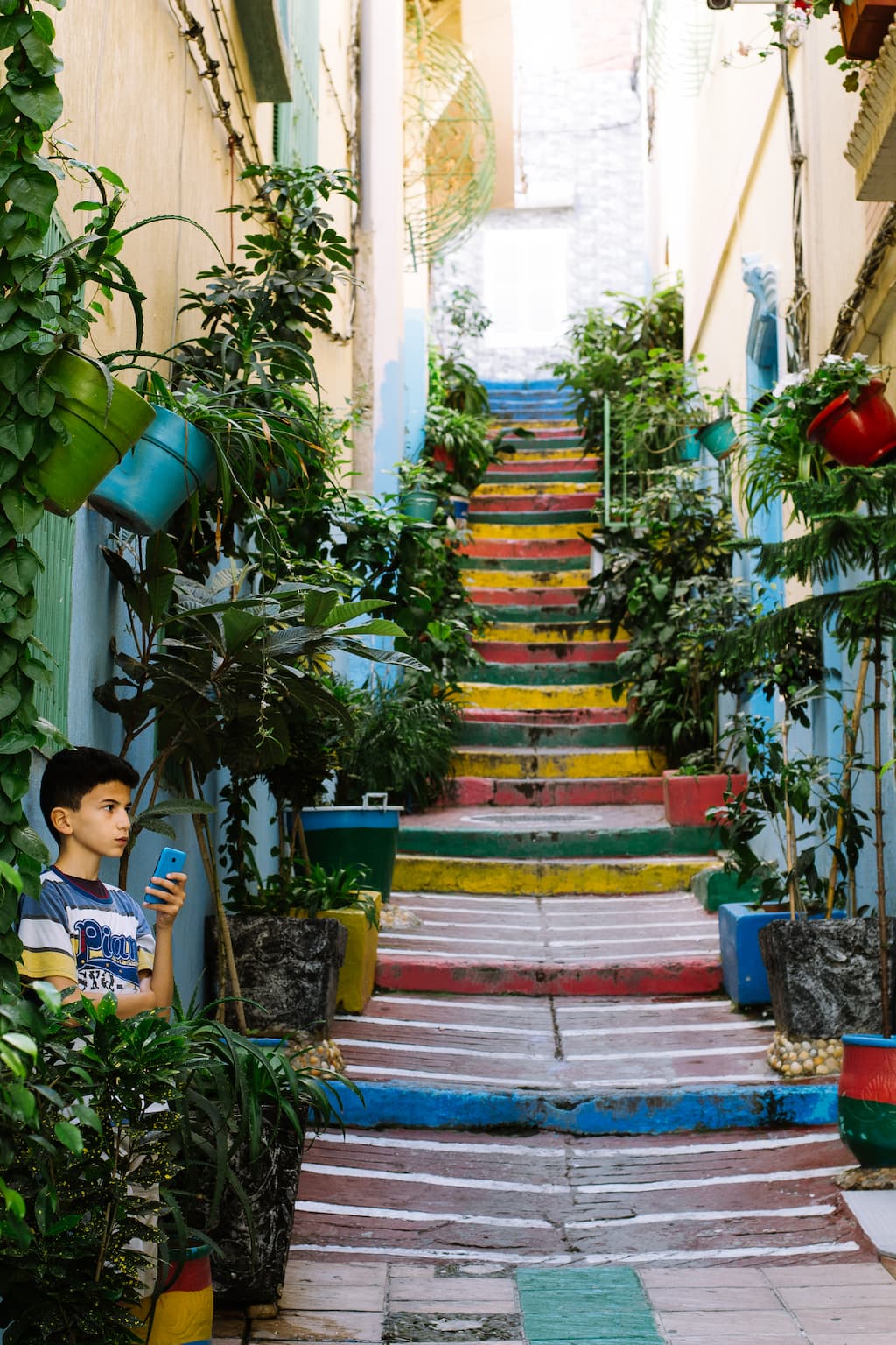 A boy on his phone at the foot of some colourful stairs