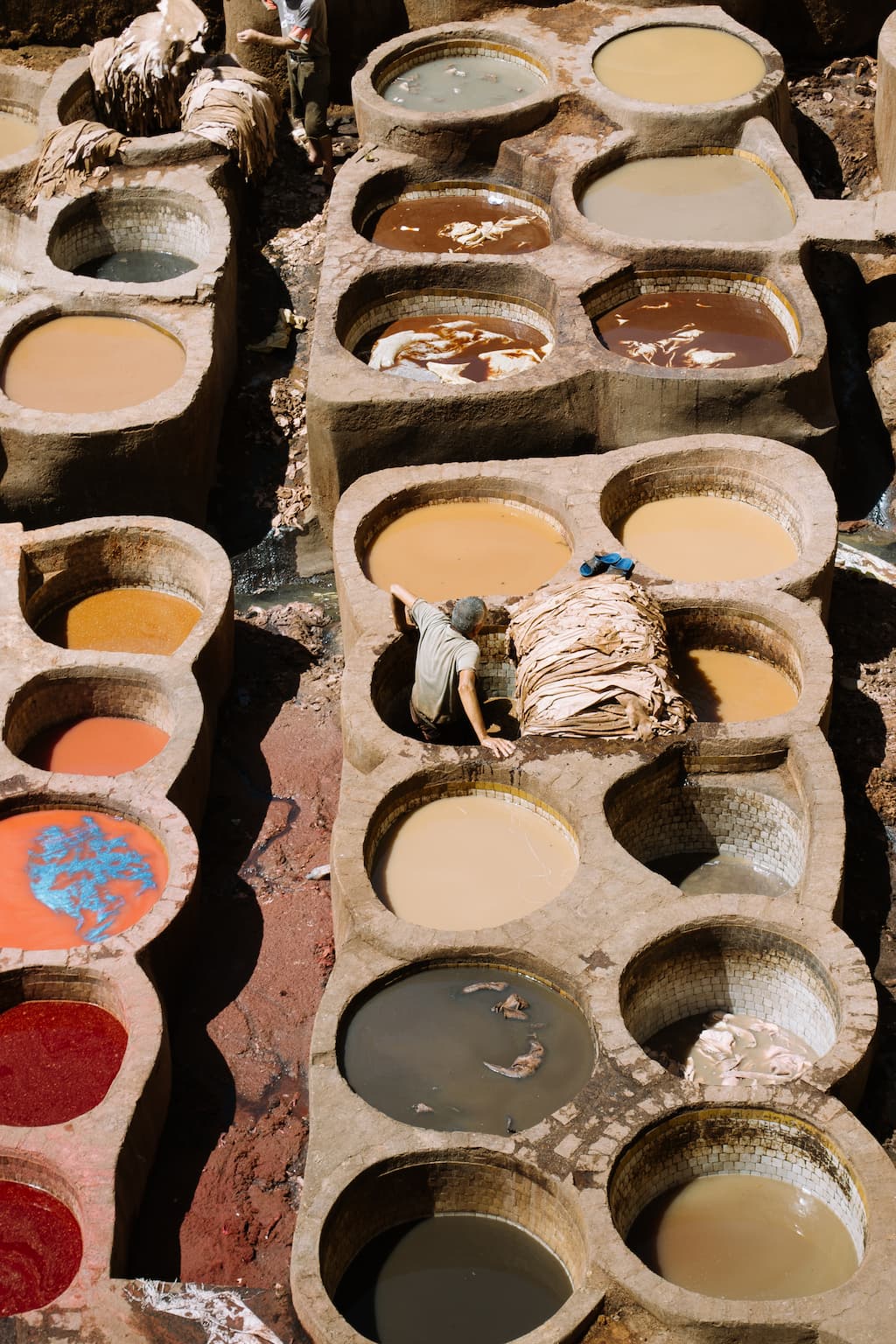 A man is half submerged in a vat of dye while working in an open air leather tannery.