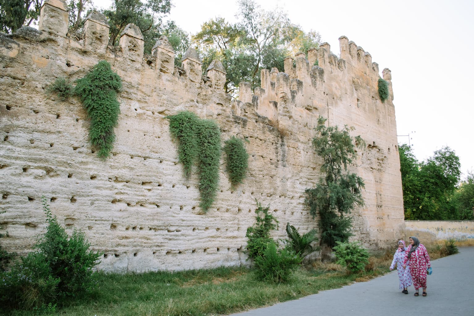 Two women walk past an old castle wall