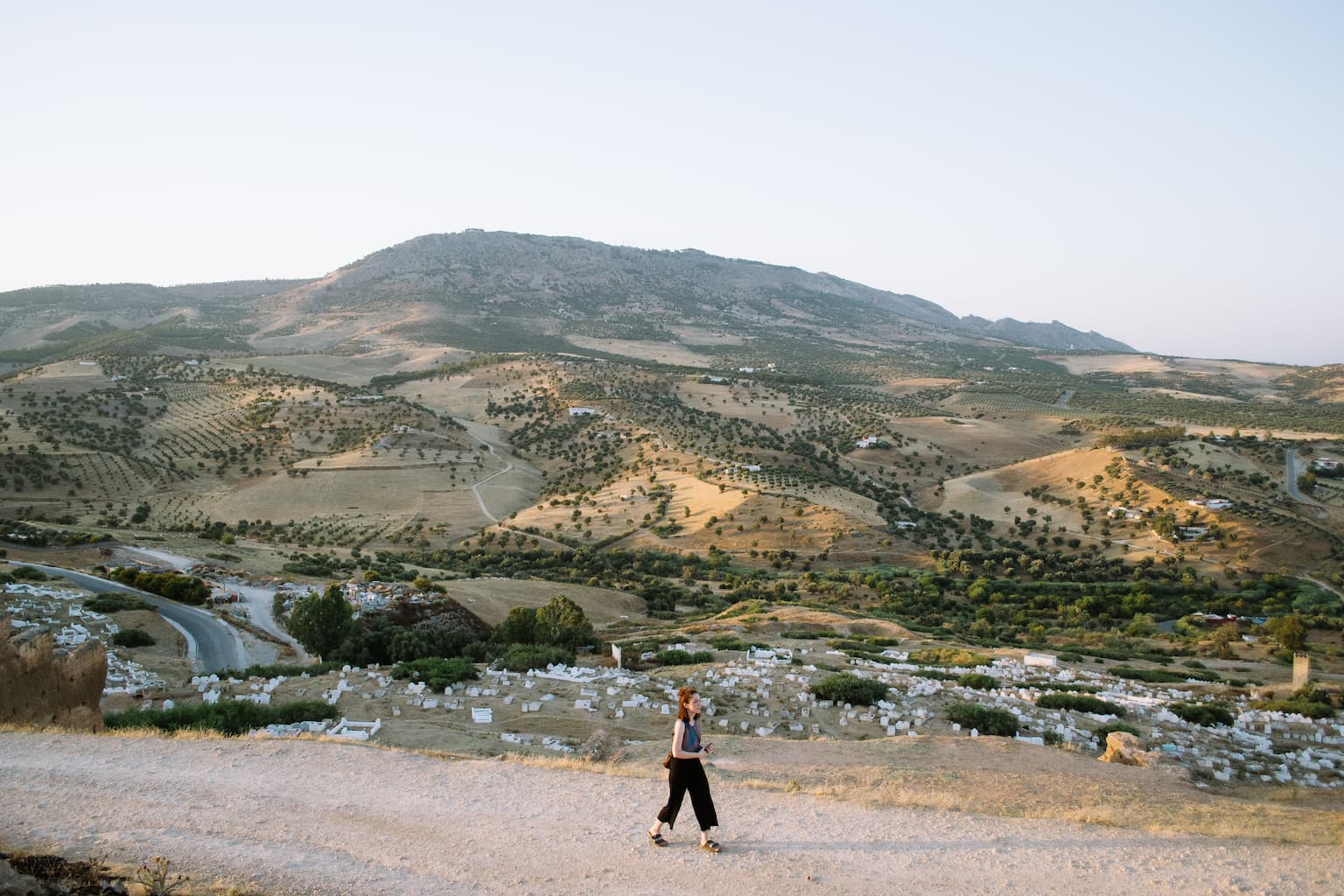 Sarah walking along a dirt road at sunset with hills in the background